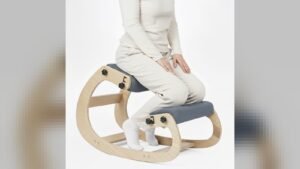 A person sitting on a kneeling chair made of natural wood with cushions, demonstrating ergonomic posture.